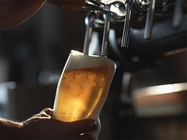 A person holding a beer glass pouring beer from a beer equipment