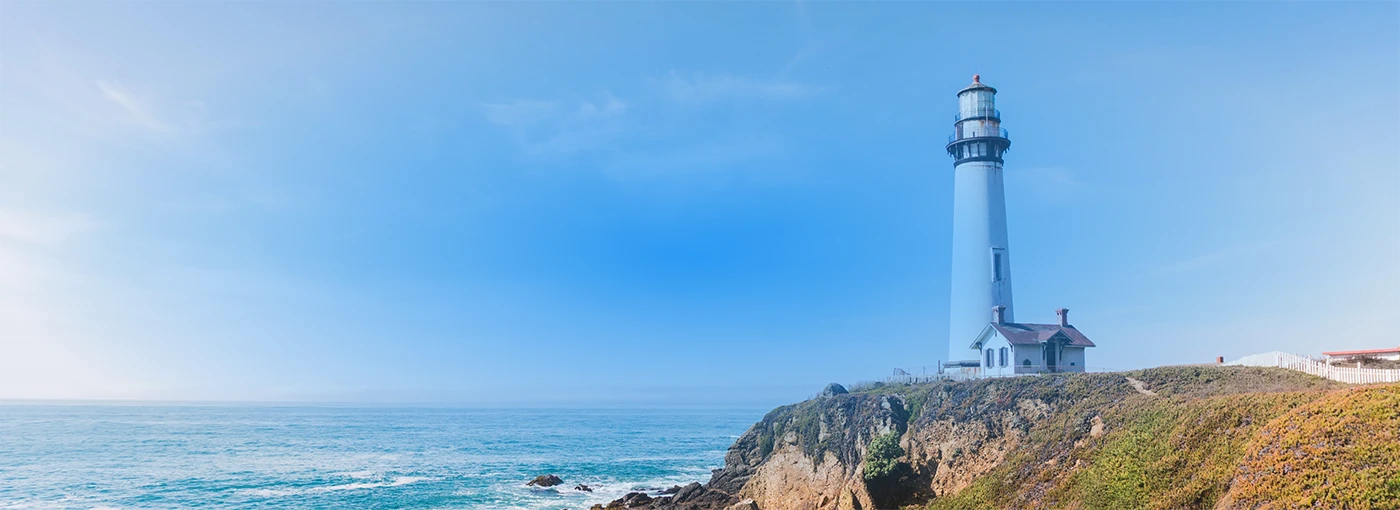 A lighthouse standing on the shore and a small house